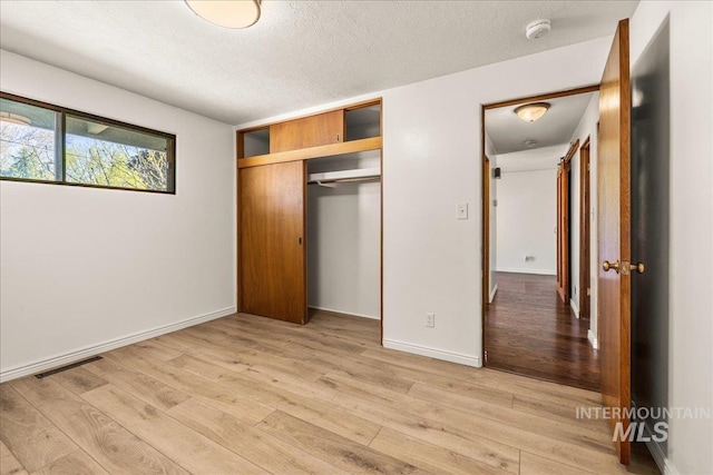 unfurnished bedroom featuring a textured ceiling, light wood-style flooring, baseboards, visible vents, and a closet
