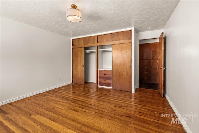 unfurnished bedroom featuring a textured ceiling, baseboards, a closet, and wood finished floors