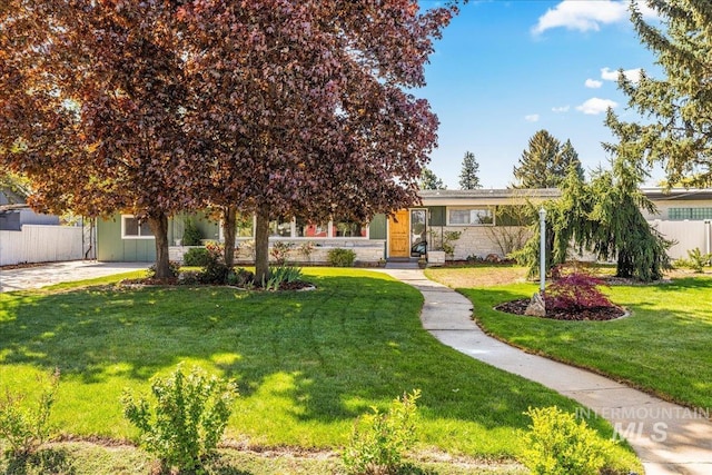 view of property hidden behind natural elements featuring fence, stone siding, and a front yard