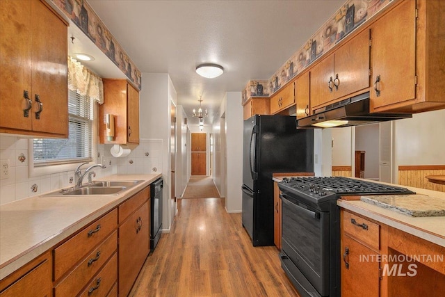 kitchen with black appliances, an inviting chandelier, sink, backsplash, and light hardwood / wood-style flooring