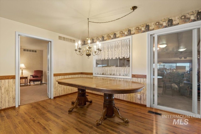 dining space with wood-type flooring, wooden walls, and an inviting chandelier