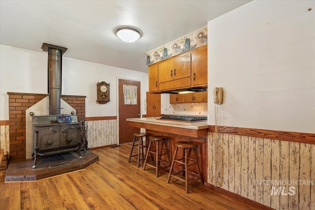 kitchen featuring hardwood / wood-style floors, kitchen peninsula, wooden walls, a kitchen breakfast bar, and a wood stove