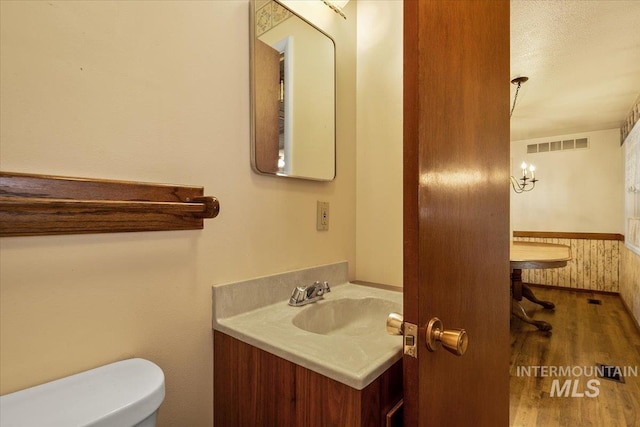 bathroom featuring toilet, wooden walls, wood-type flooring, a textured ceiling, and vanity