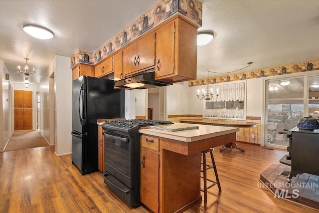 kitchen featuring pendant lighting, black appliances, a breakfast bar, a textured ceiling, and a wood stove