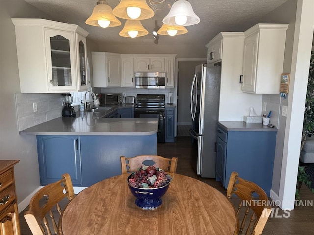 kitchen with appliances with stainless steel finishes, glass insert cabinets, a sink, blue cabinets, and a peninsula