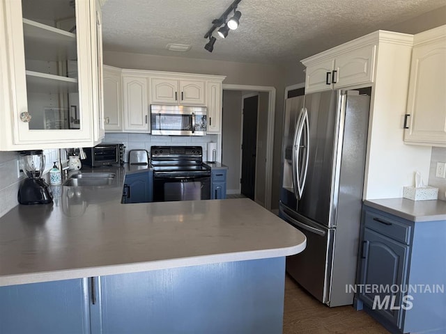 kitchen with tasteful backsplash, appliances with stainless steel finishes, glass insert cabinets, a peninsula, and a textured ceiling