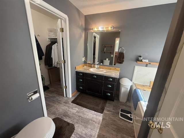 full bath featuring toilet, a walk in closet, and vanity