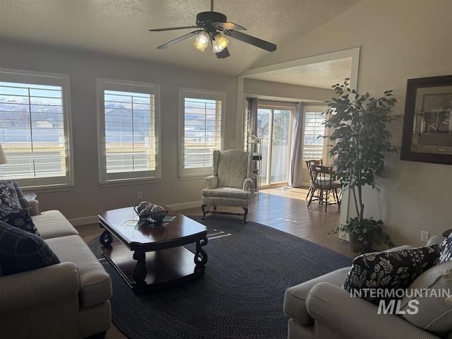 living room featuring a ceiling fan, vaulted ceiling, a textured ceiling, wood finished floors, and baseboards