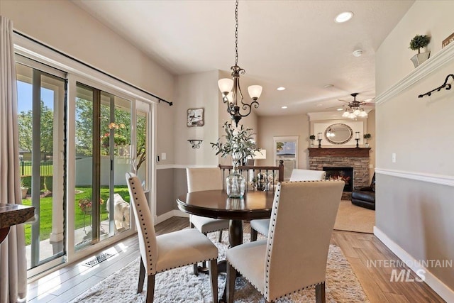 dining space with ceiling fan, baseboards, recessed lighting, a stone fireplace, and light wood-type flooring