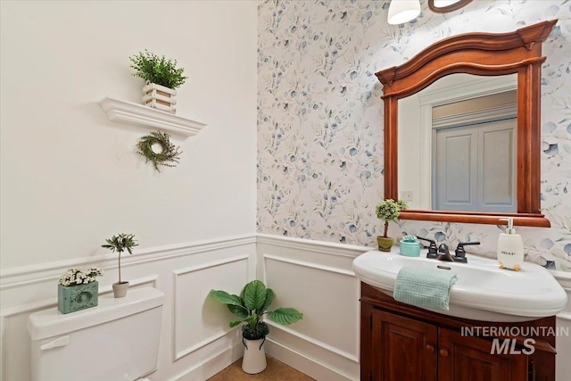 half bath featuring wainscoting, vanity, wallpapered walls, toilet, and a decorative wall