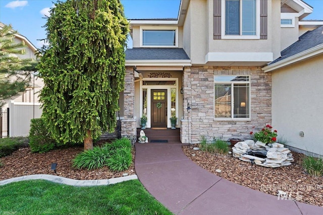 doorway to property featuring stone siding, stucco siding, roof with shingles, and fence