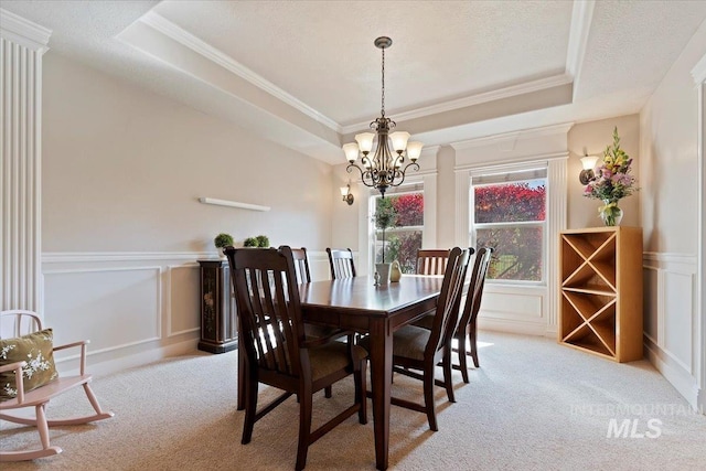 dining room featuring a raised ceiling, light colored carpet, a chandelier, a decorative wall, and crown molding