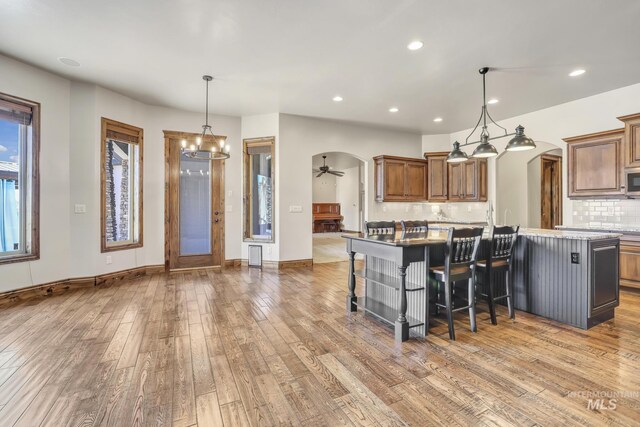 kitchen with recessed lighting, arched walkways, an island with sink, backsplash, and light wood-type flooring
