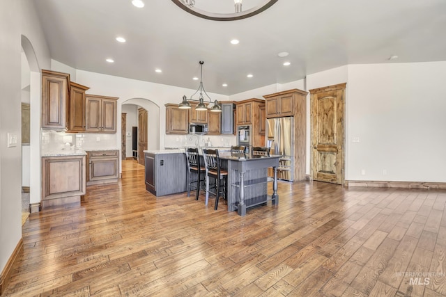 kitchen featuring appliances with stainless steel finishes, brown cabinets, light wood finished floors, and arched walkways