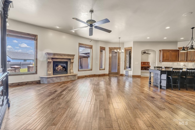 living area with recessed lighting, wood finished floors, ceiling fan with notable chandelier, and a lit fireplace