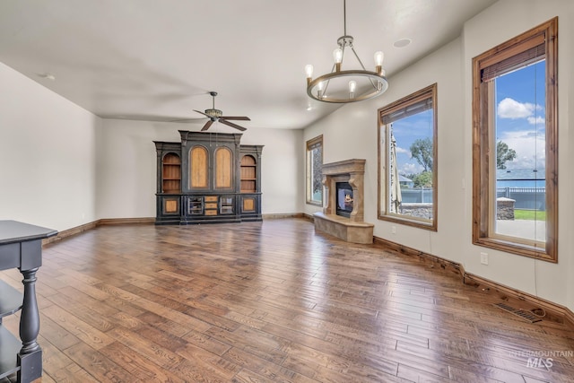 unfurnished living room featuring a wealth of natural light, hardwood / wood-style floors, baseboards, and ceiling fan with notable chandelier
