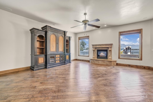 unfurnished living room with baseboards, a ceiling fan, wood-type flooring, and a glass covered fireplace