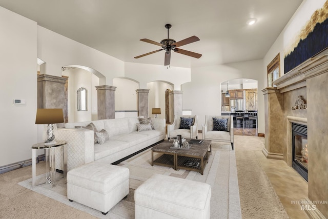 carpeted living room with baseboards, arched walkways, ceiling fan, and a fireplace