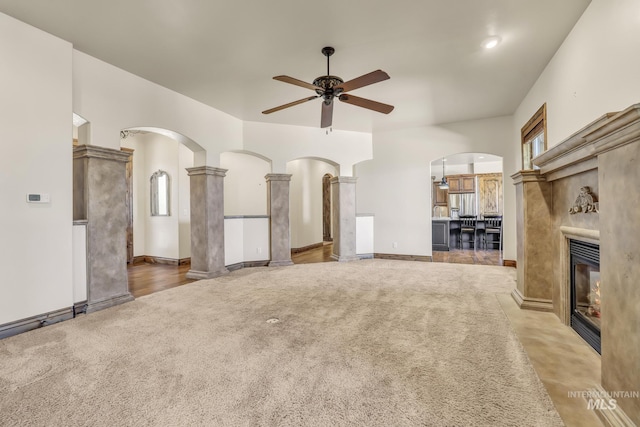 unfurnished living room with arched walkways, ceiling fan, carpet, and a glass covered fireplace
