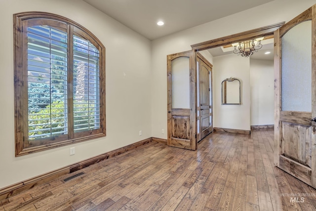 empty room featuring recessed lighting, wood-type flooring, a notable chandelier, visible vents, and baseboards
