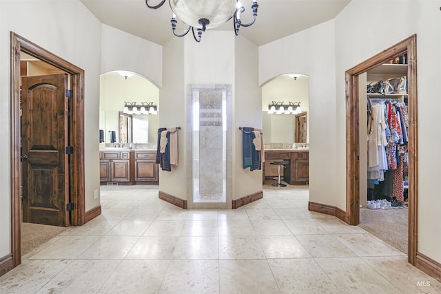 hallway with an inviting chandelier, light tile patterned floors, baseboards, and arched walkways