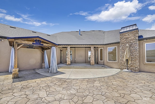 back of property featuring stone siding, stucco siding, and a patio area