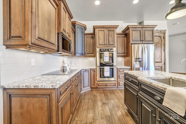 kitchen with light stone counters, tasteful backsplash, a sink, appliances with stainless steel finishes, and light wood finished floors