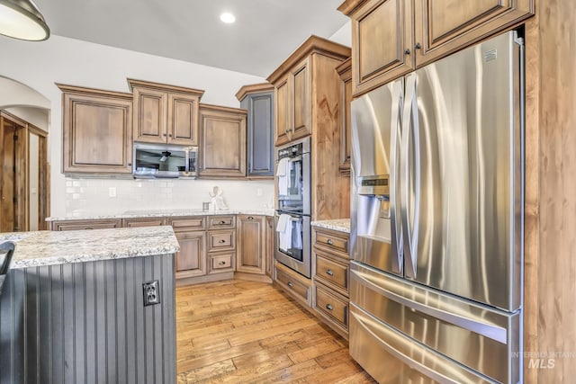 kitchen featuring tasteful backsplash, light stone countertops, arched walkways, light wood-style flooring, and stainless steel appliances