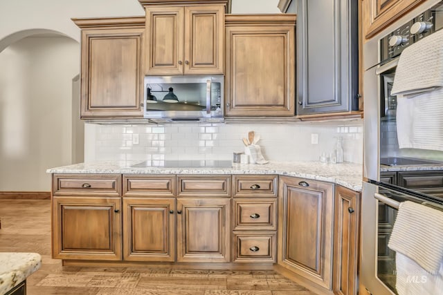 kitchen featuring tasteful backsplash, light stone counters, baseboards, arched walkways, and appliances with stainless steel finishes