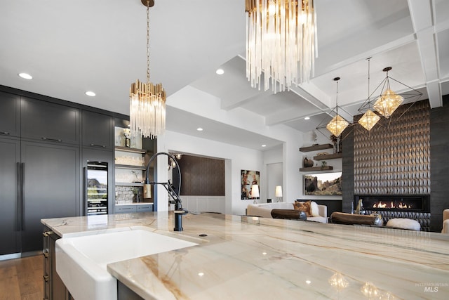 kitchen with light stone counters, a large fireplace, sink, pendant lighting, and beamed ceiling