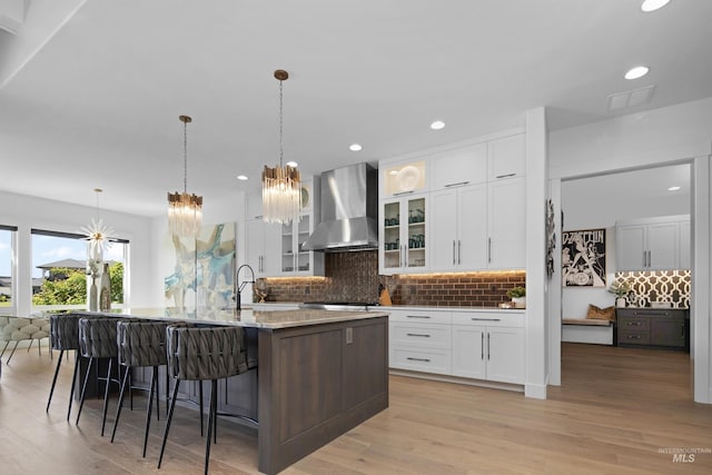 kitchen featuring white cabinets, sink, an island with sink, and wall chimney range hood