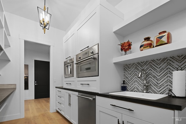 kitchen with pendant lighting, oven, sink, light hardwood / wood-style floors, and white cabinetry