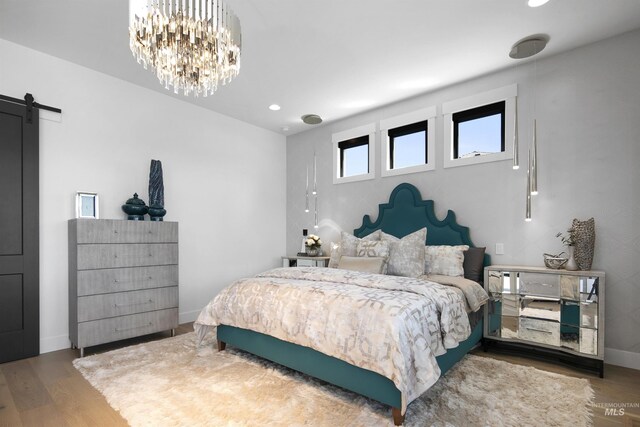 bedroom with a barn door, a notable chandelier, and hardwood / wood-style flooring