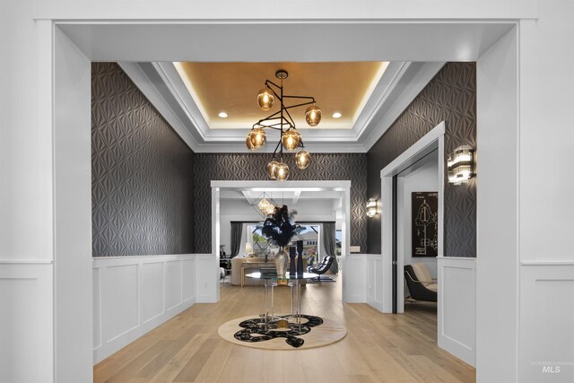 corridor with a raised ceiling, light hardwood / wood-style flooring, and an inviting chandelier