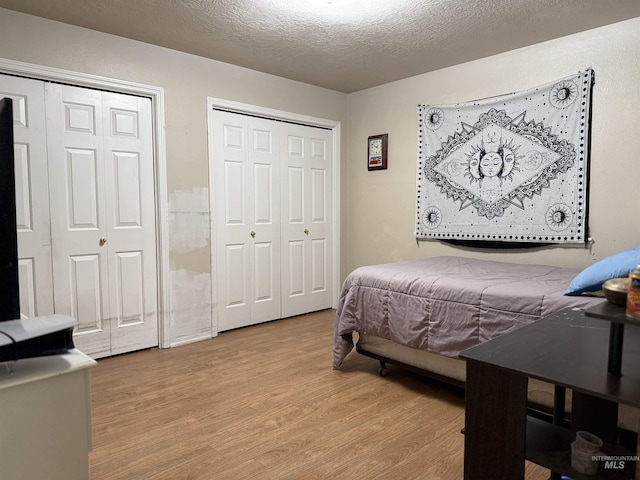 bedroom with light hardwood / wood-style floors, a textured ceiling, and two closets