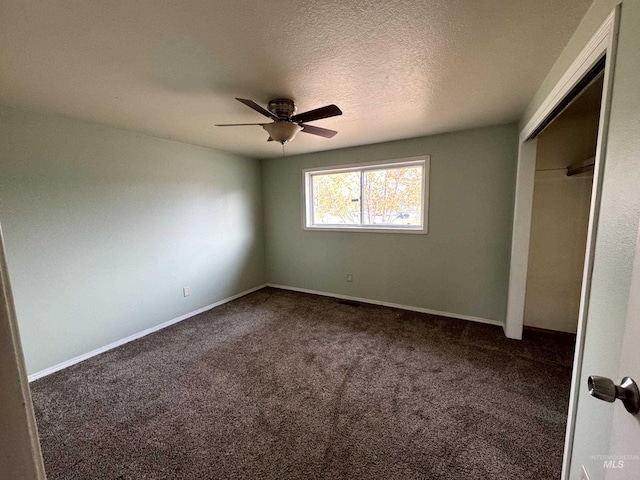 unfurnished bedroom featuring ceiling fan, dark carpet, a textured ceiling, and a closet