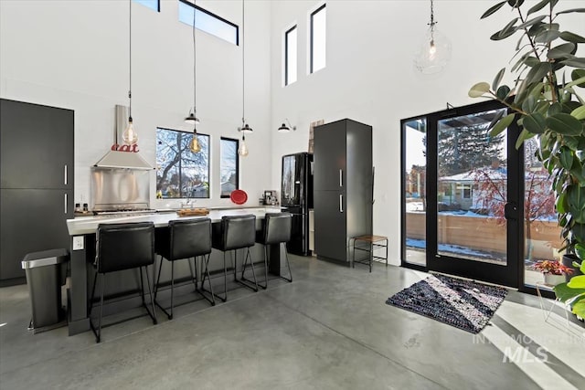 kitchen with a kitchen island, black refrigerator, pendant lighting, ventilation hood, and a kitchen breakfast bar