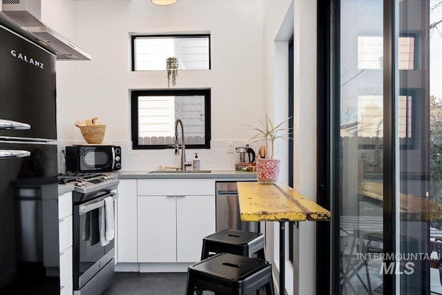kitchen with sink, white cabinets, backsplash, black appliances, and wall chimney exhaust hood