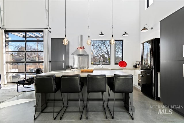 kitchen with sink, black refrigerator, hanging light fixtures, white cabinetry, and a center island