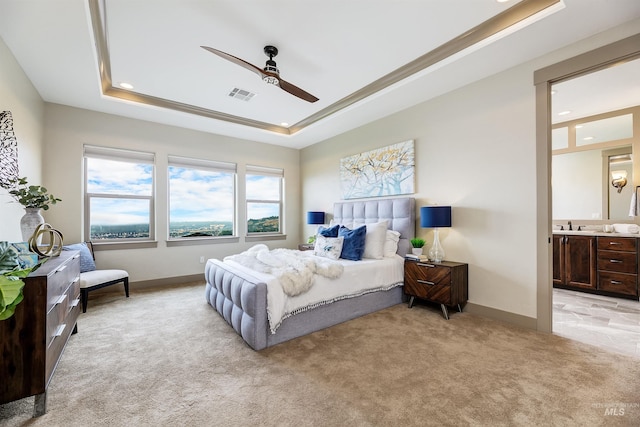 bedroom with connected bathroom, a tray ceiling, light colored carpet, and ceiling fan