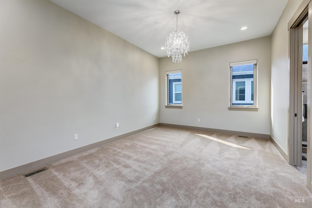 spare room with a chandelier, light colored carpet, and a wealth of natural light