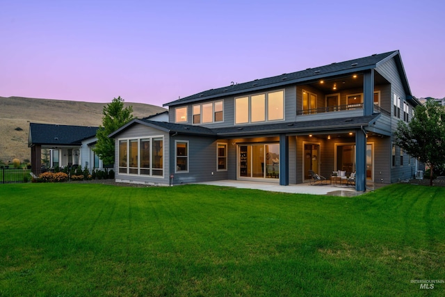 back house at dusk with a patio, a balcony, and a yard