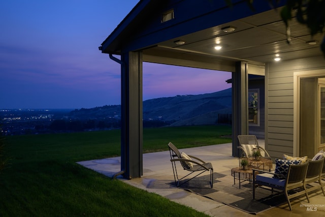 patio terrace at dusk featuring a mountain view and a yard