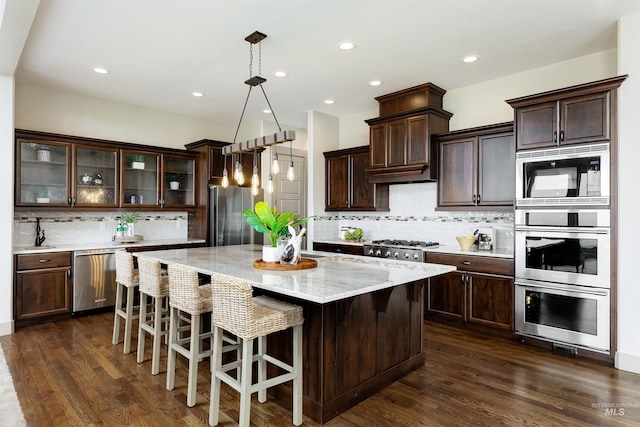 kitchen with appliances with stainless steel finishes, dark hardwood / wood-style flooring, tasteful backsplash, and a center island