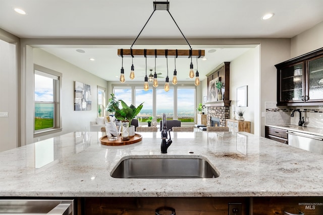 kitchen with backsplash, light stone counters, a stone fireplace, and a wealth of natural light