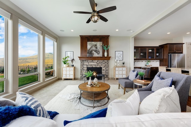 carpeted living room with ceiling fan and a stone fireplace