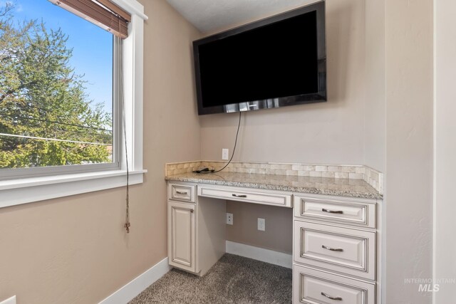 unfurnished office featuring built in study area, baseboards, and light carpet