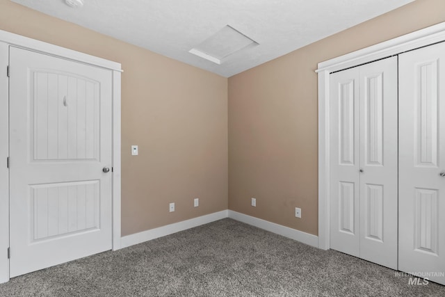 unfurnished bedroom with attic access, carpet, a closet, and baseboards