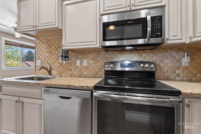 kitchen featuring light stone counters, stainless steel appliances, a sink, tasteful backsplash, and white cabinetry