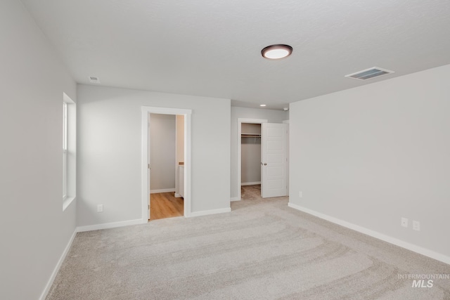 unfurnished bedroom featuring connected bathroom, a spacious closet, light colored carpet, and a closet